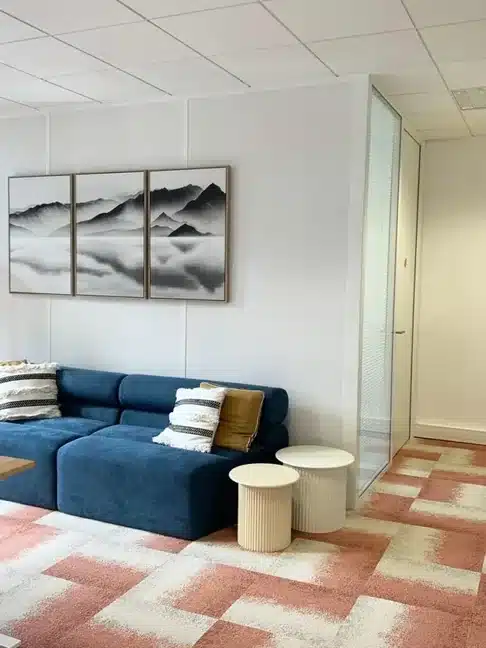 Espace détente de bureau aménagé par Melvi Intérieur avec canapé bleu, tables basses et décoration murale contemporaine